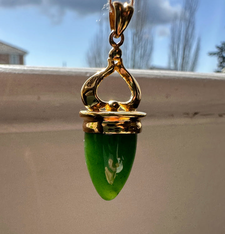 Gold-tone pendant with green jade teardrop hanging in front of a window.