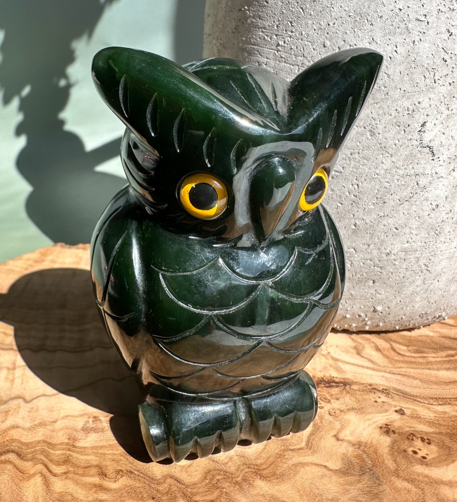 Dark green jade owl figurine with yellow eyes perched on a wooden surface