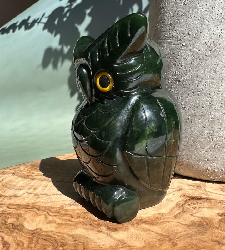 Dark green jade owl figurine with a yellow eye sits on a carved wood surface