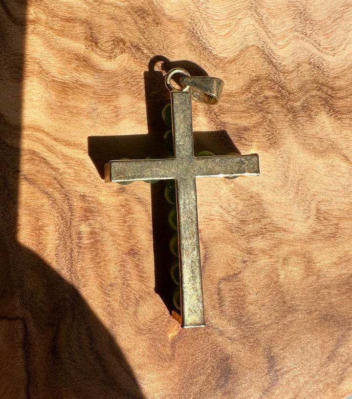 Jade bead cross pendant resting on wood, showing metal frame and bail