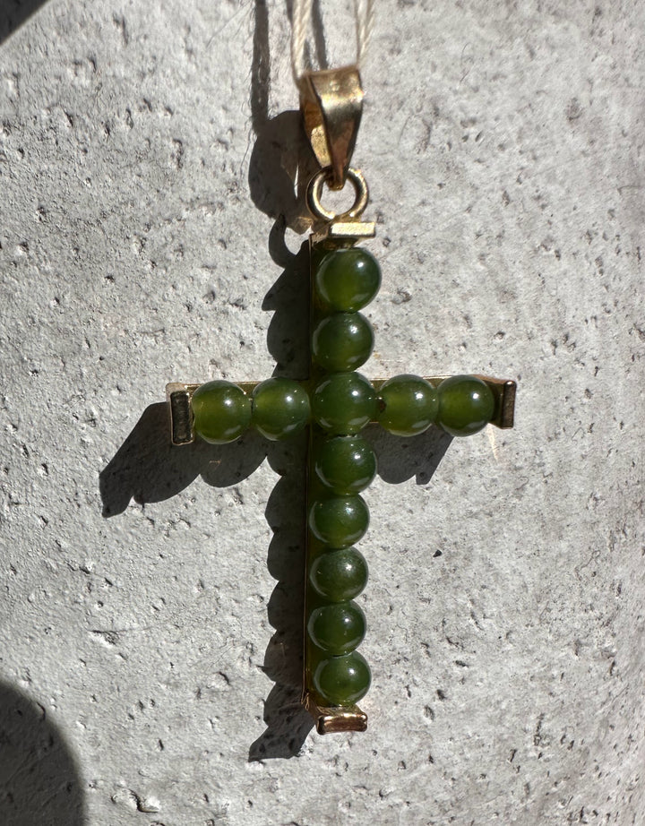 Close up of jade bead cross pendant against a textured stone surface with green beads forming cross