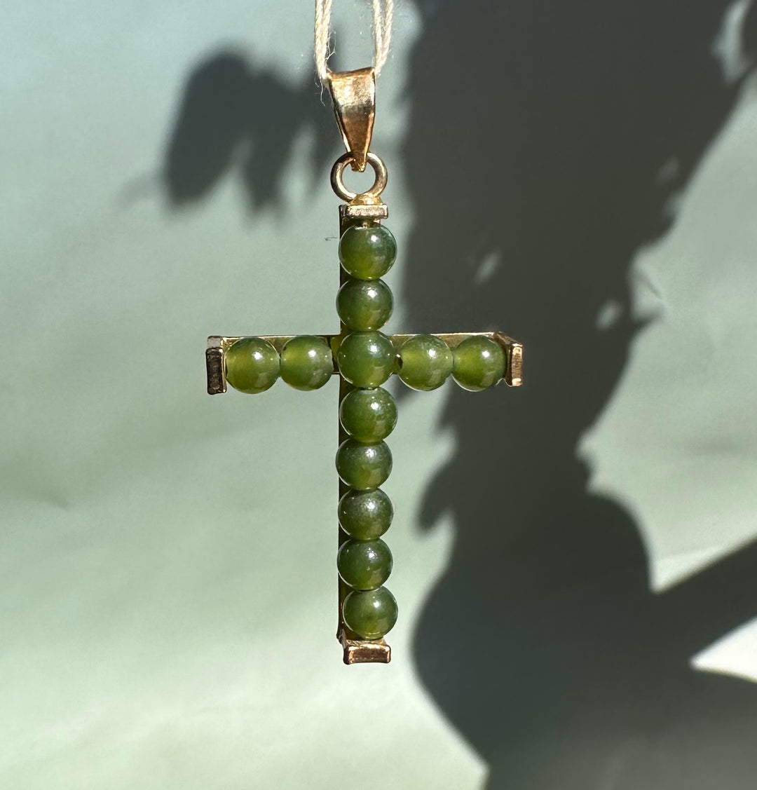 Vintage jade bead cross pendant with gold setting hanging from a cord