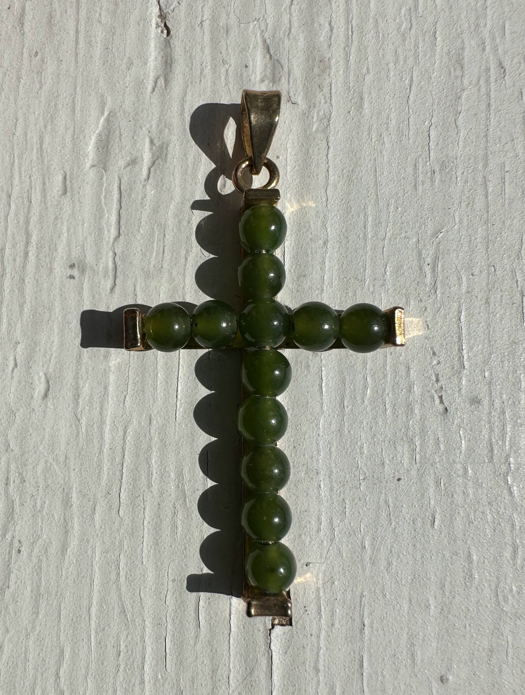 Vintage jade cross pendant formed by green beads set in metal with a bail at the top.