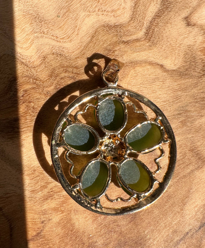 Circular vintage pendant with five green jade petals forming a flower inside a gold frame.