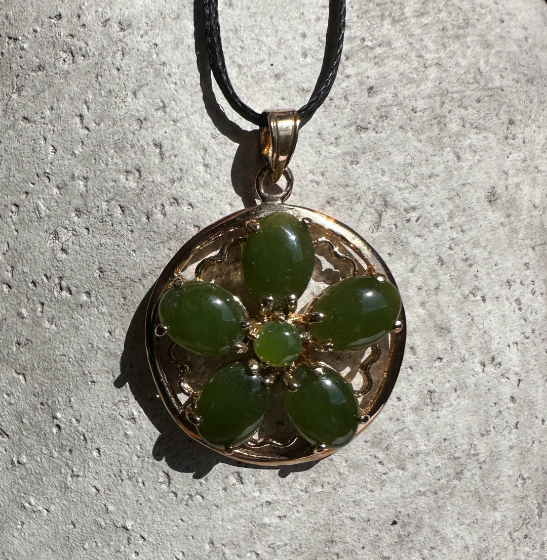 Close up of round vintage jade flower pendant with green stones set in an ornate gold frame.