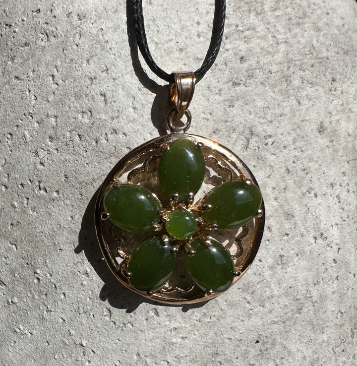 Close up of round vintage jade flower pendant with green stones set in an ornate gold frame.
