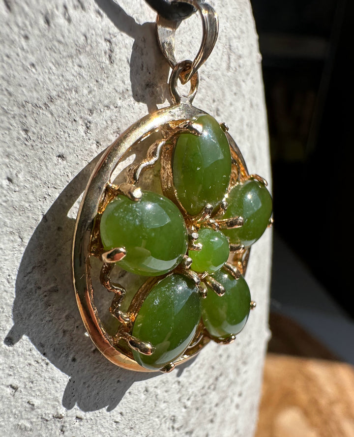 Jade flower pendant on a black cord, jade stones set in a gold circular frame.