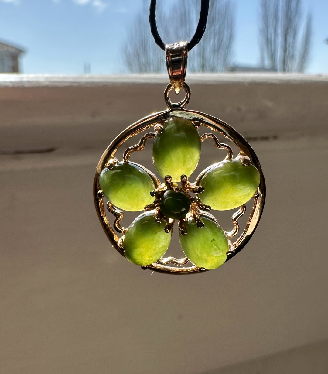 Jade flower pendant on a black cord necklace with a gold circular frame and five oval green jade petals