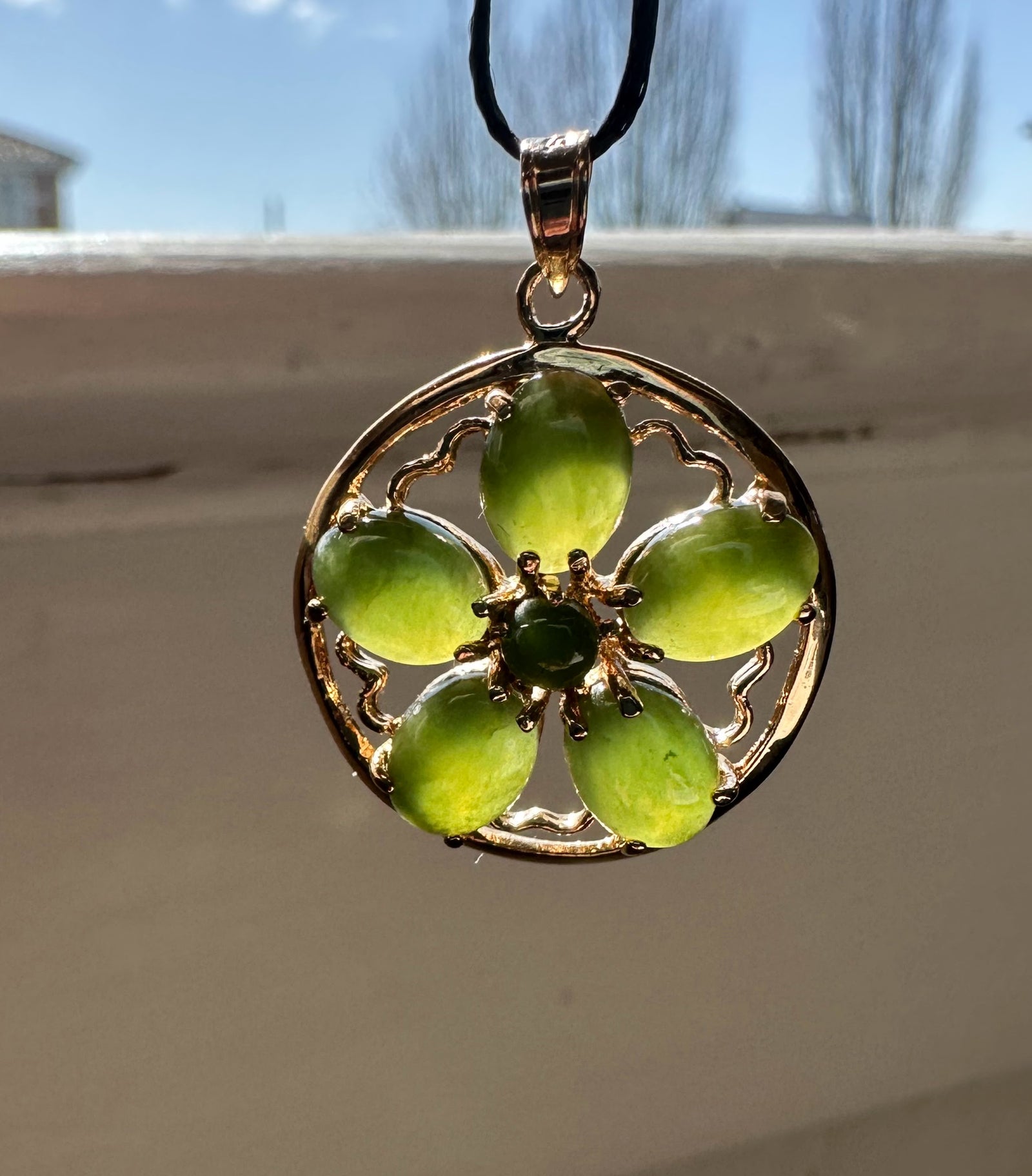 Jade flower pendant on a black cord necklace with a gold circular frame and five oval green jade petals