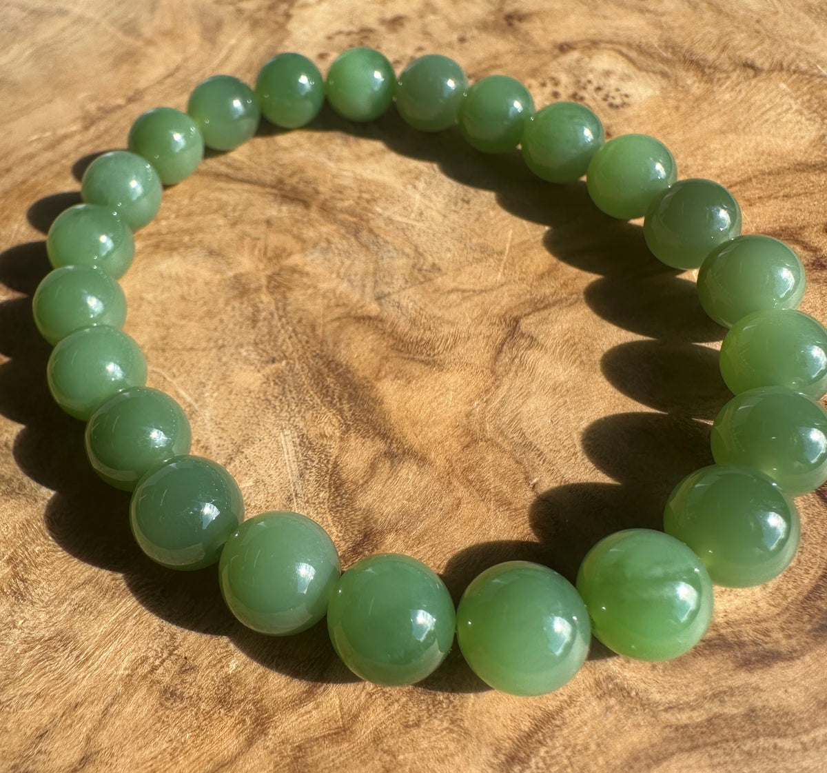 A beaded stretch bracelet made of smooth, polished green jade-like round beads, displayed on a textured wooden surface.