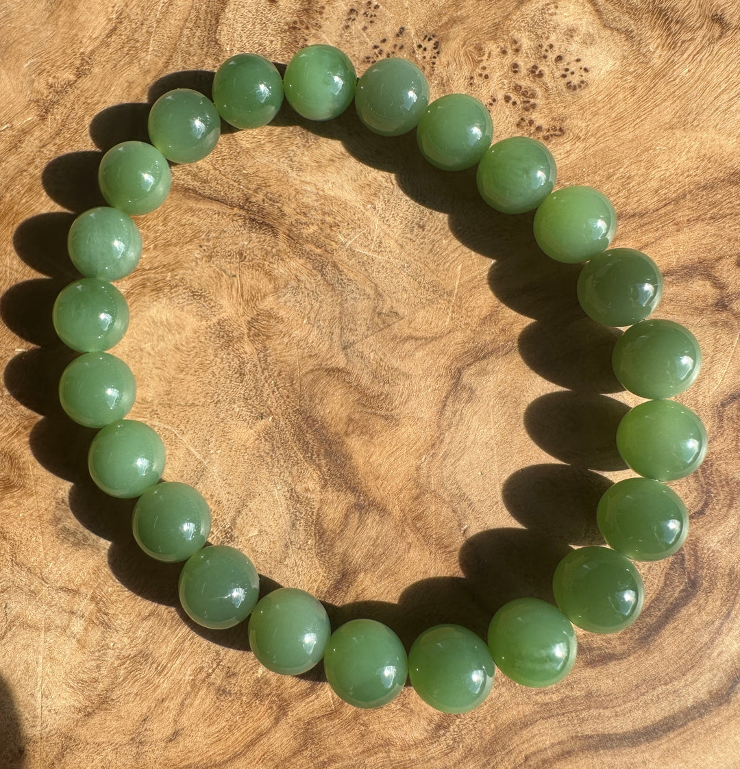 A beaded stretch bracelet made of smooth, polished green jade-like round beads, displayed on a textured wooden surface.