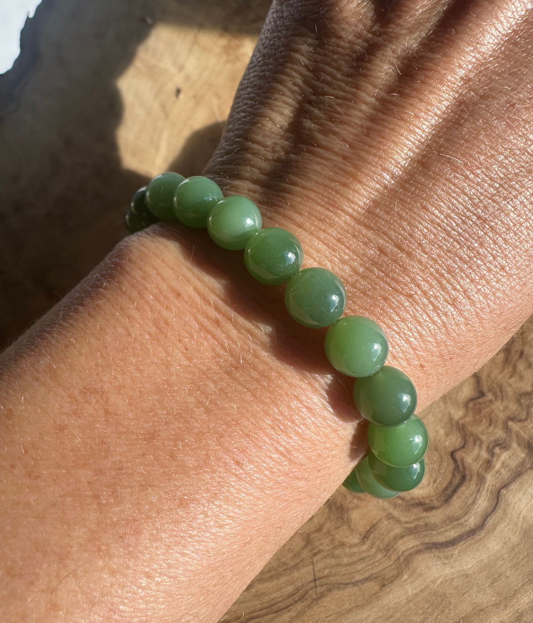 A green beaded bracelet made of smooth, polished round beads worn on a person&