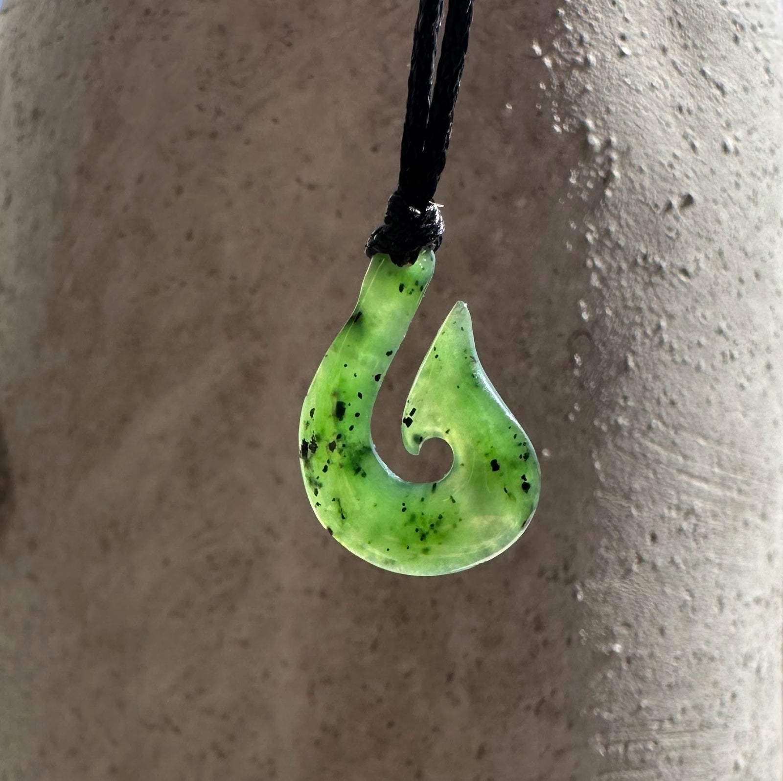 Green jade fishhook pendant with curved spiral cutout on a black cord