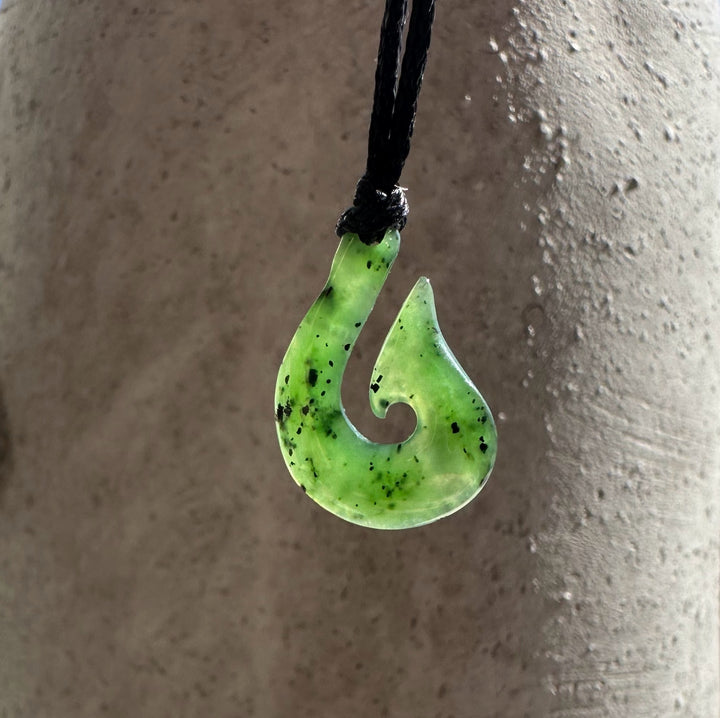 Green jade fishhook pendant with curved spiral cutout on a black cord