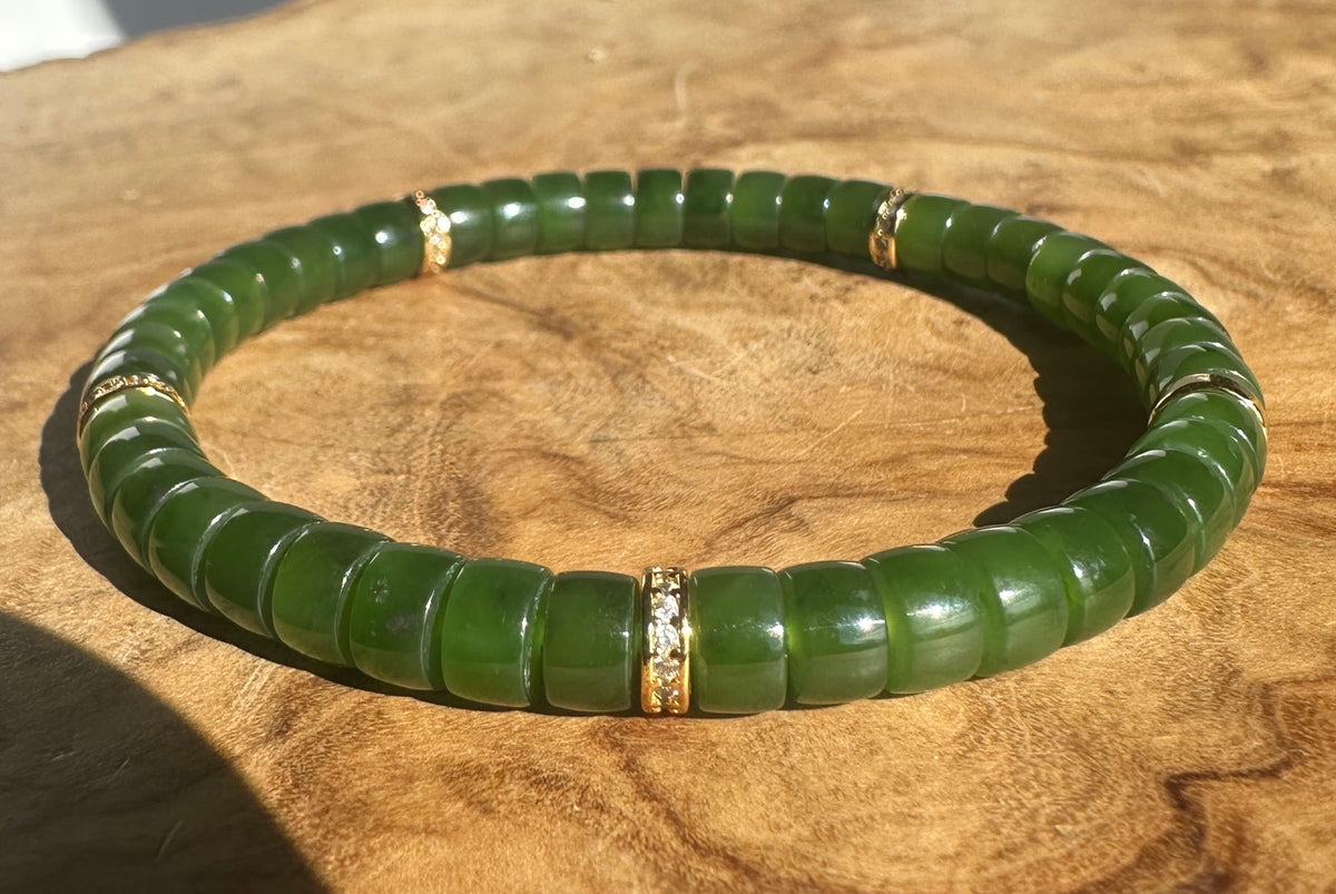 A green beaded stretch bracelet with gold spacer rings, displayed on a textured wooden surface.