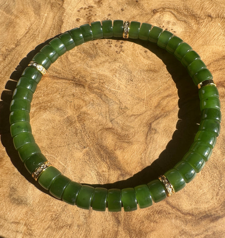 A green jade beaded bracelet with small gold spacer rings, displayed on a textured wooden surface.
