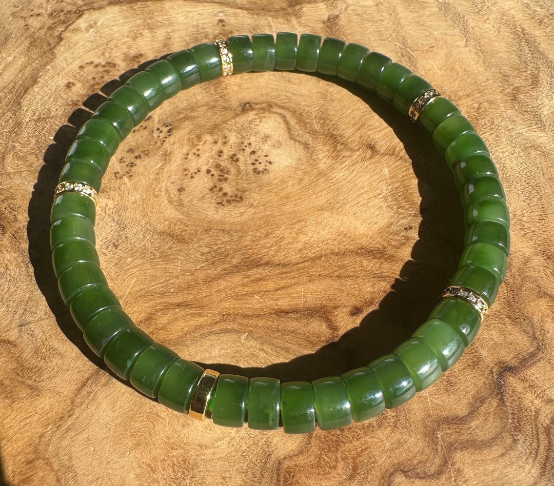 A green jade beaded bracelet with small gold spacer accents, displayed on a textured wooden surface.