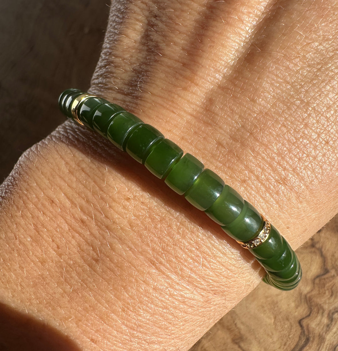 A green beaded bracelet with gold accents, shown worn on a person&