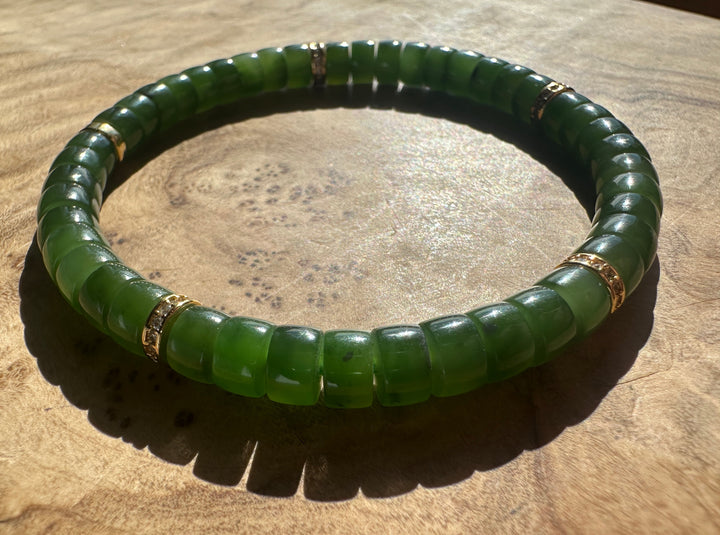 A green beaded bracelet with gold spacer rings, displayed on a textured wooden surface.
