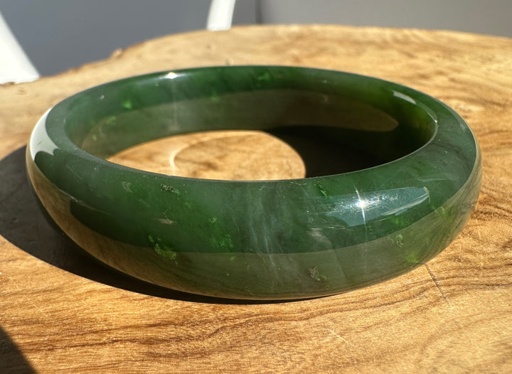 A polished dark green jade bangle bracelet resting on a rustic wooden surface.