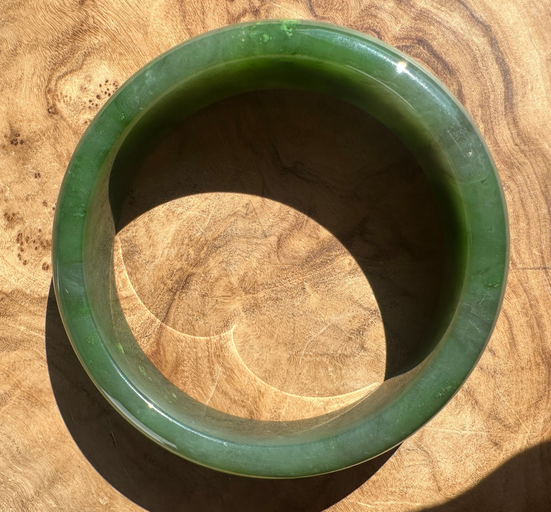 A round green jade bangle bracelet displayed on a textured wooden surface.
