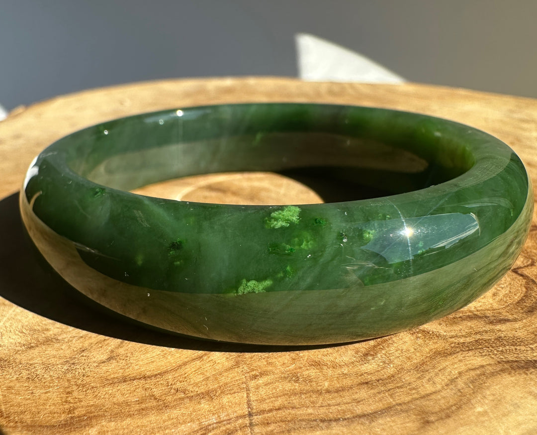 A polished green jade bangle bracelet displayed on a round wooden surface.