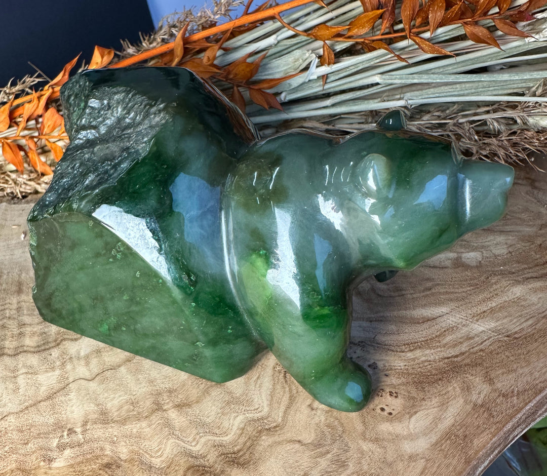 Green polar jade bear sculpture resting on a wooden surface with dried orange foliage in the background
