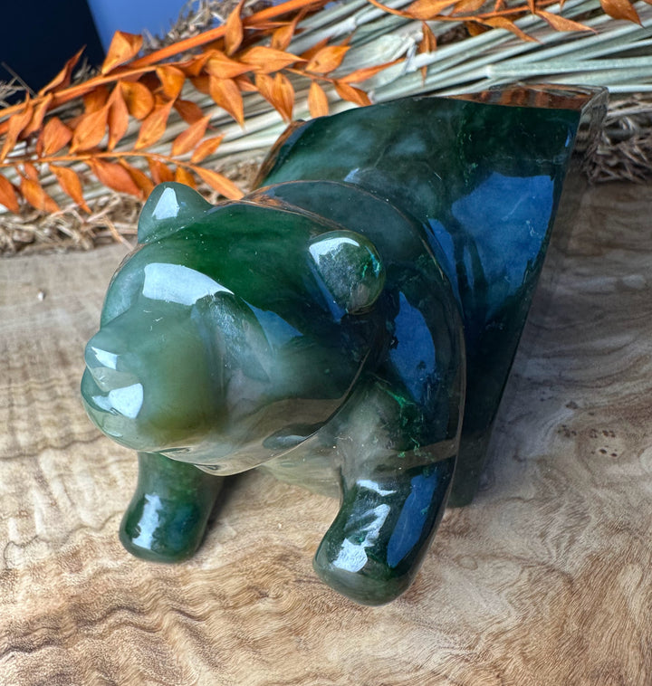 Green polar jade bear emerging sculpture viewed from a front left angle on a wooden surface with dried stems nearby