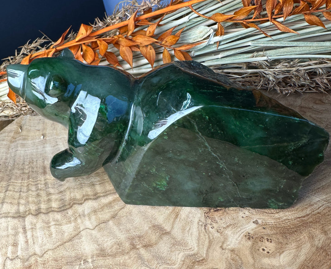 Green Polar Jade bear emerging sculpture resting on a wooden surface with dried orange foliage in the background.