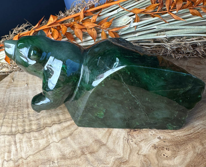 Green Polar Jade bear emerging sculpture resting on a wooden surface with dried orange foliage in the background.