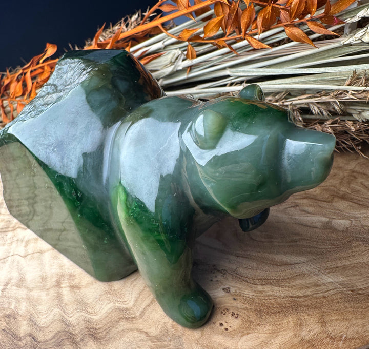 Green polar jade bear emerging sculpture shown from a side angle on wood with dried plant stalks in the background