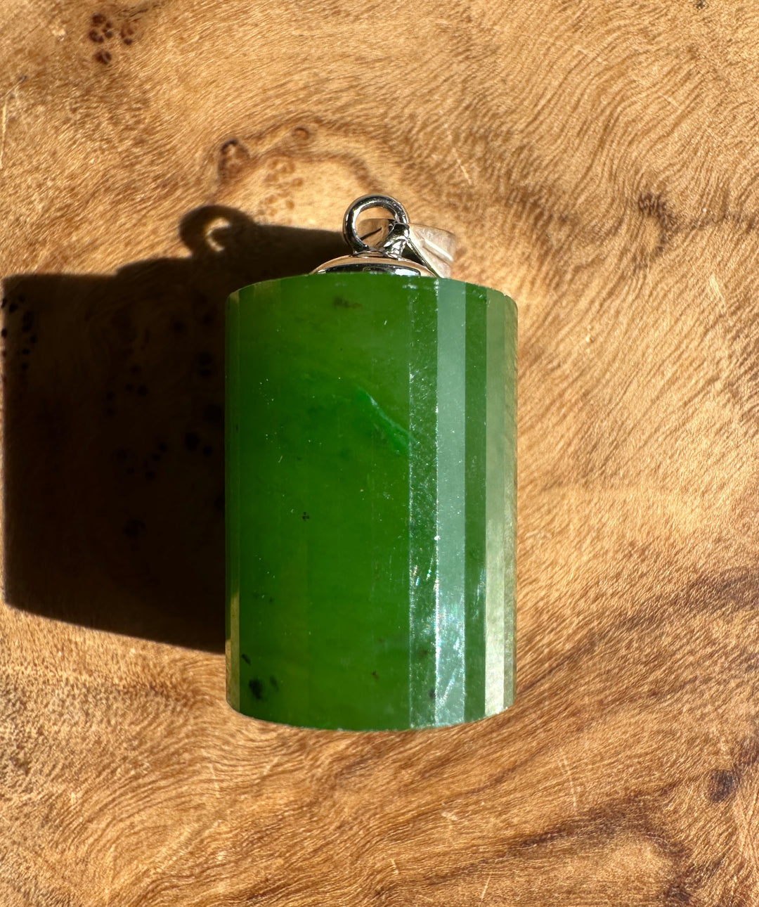 Close up of a green jade faceted pendant with a silver bail on a wood surface.