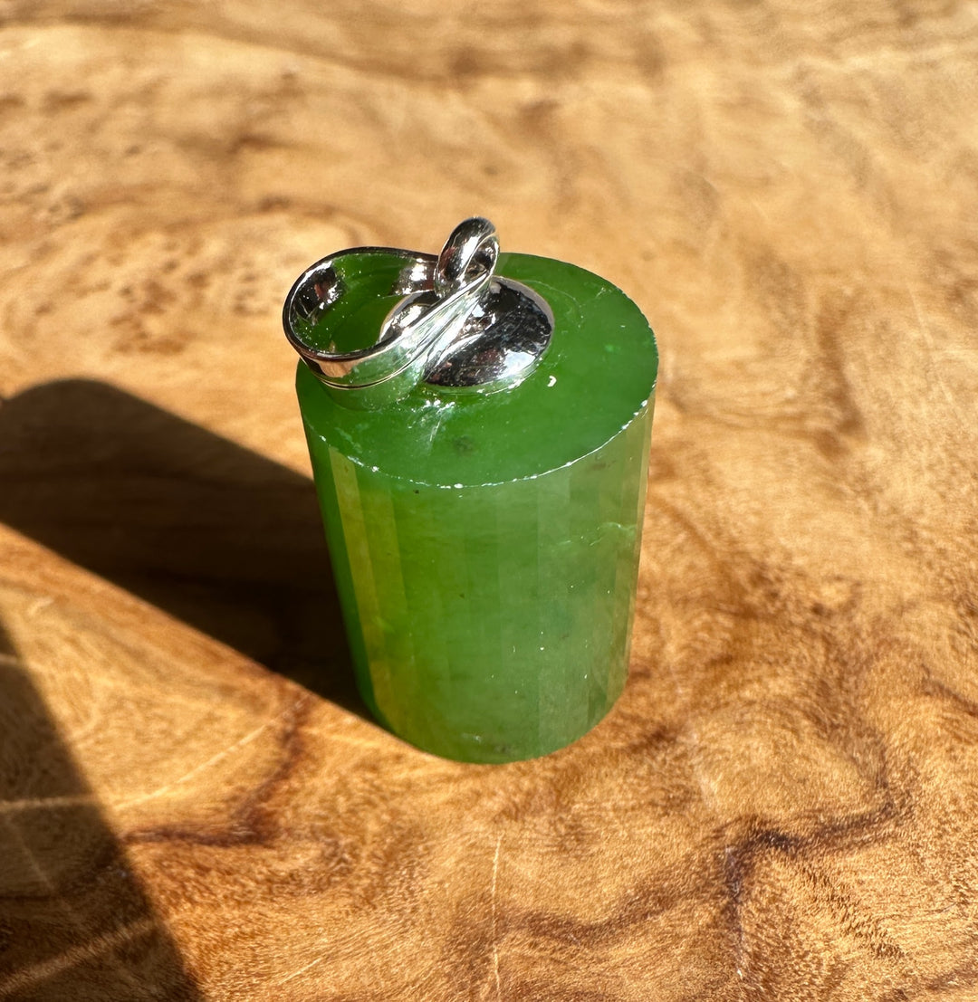 Silver bail and green jade pendant on a chain against a wood background.
