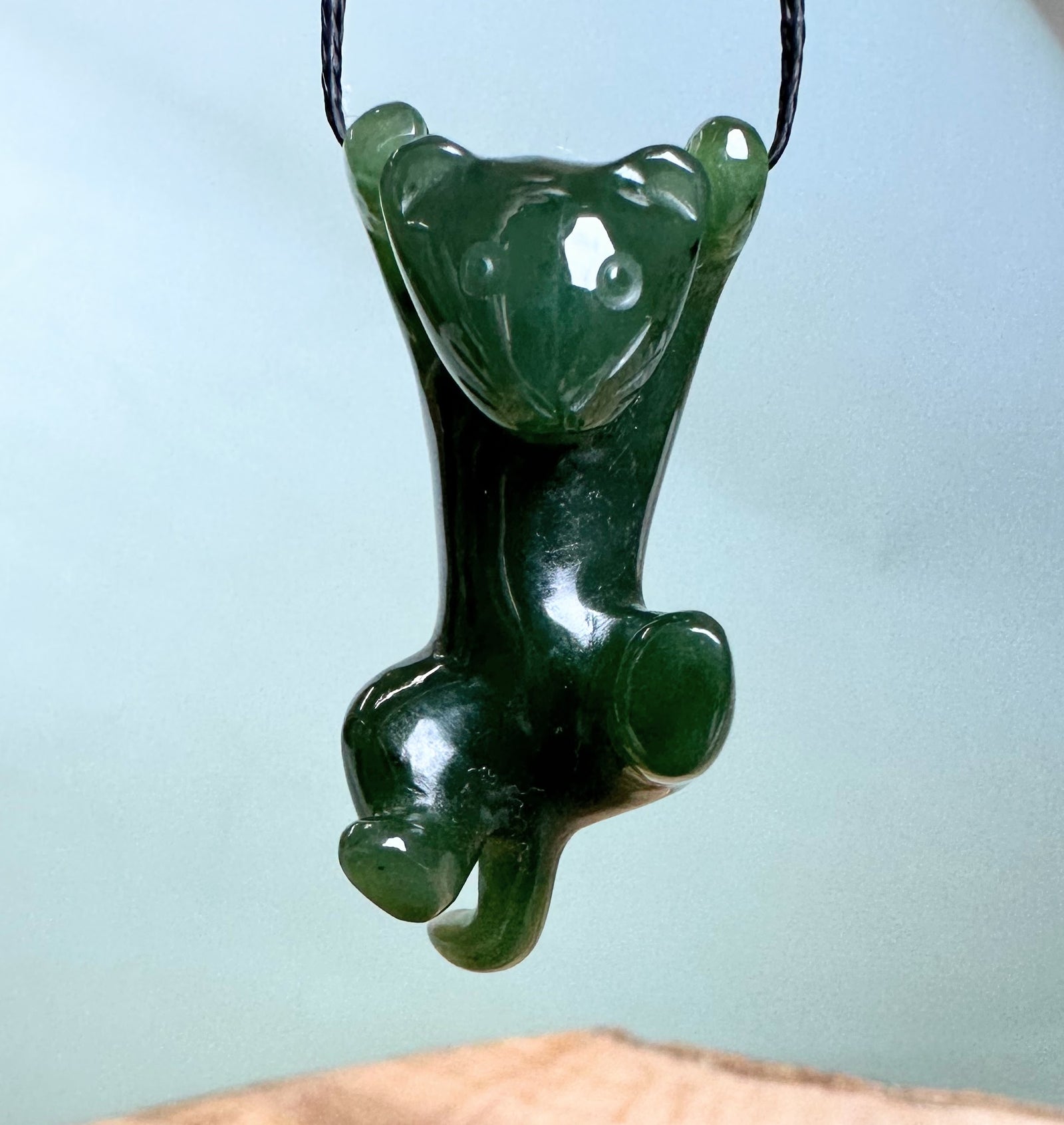 Green jade cat pendant hanging from a black cord