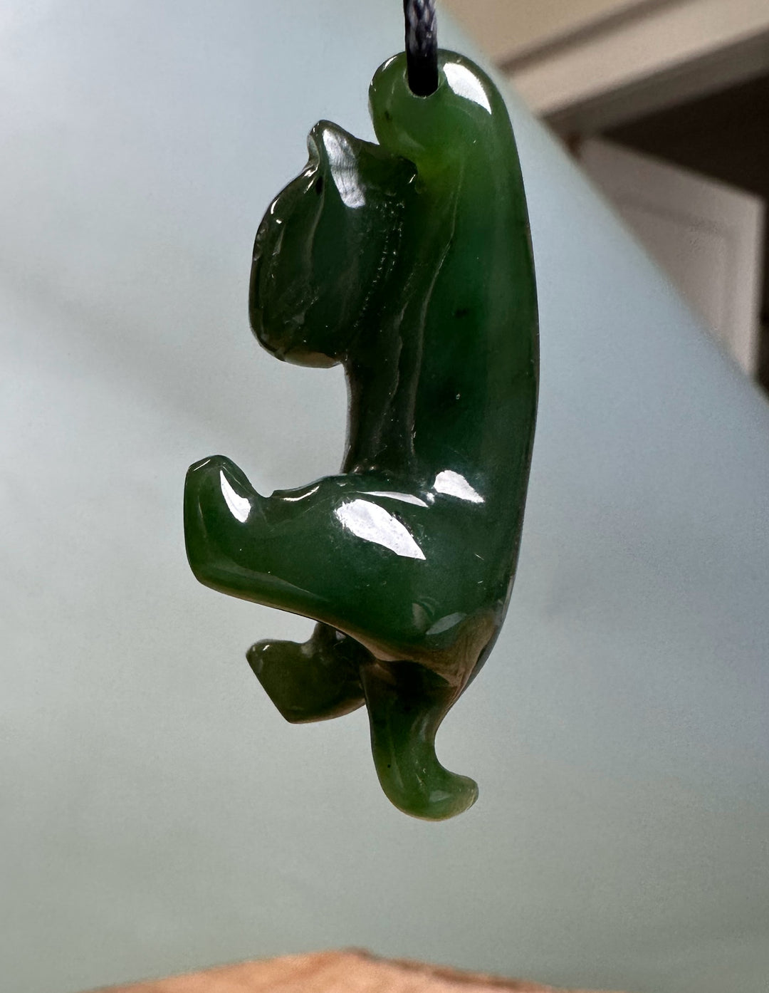 Side view of green cat pendant on a cord showing a curved body