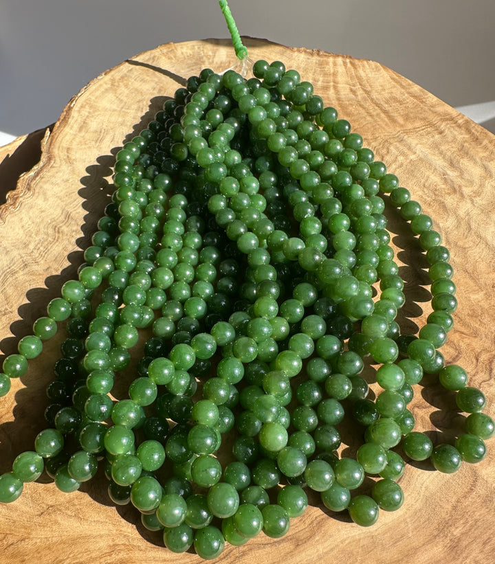 Green Canadian Nephrite Jade Unstrung Beads on a wooden base in sunlight