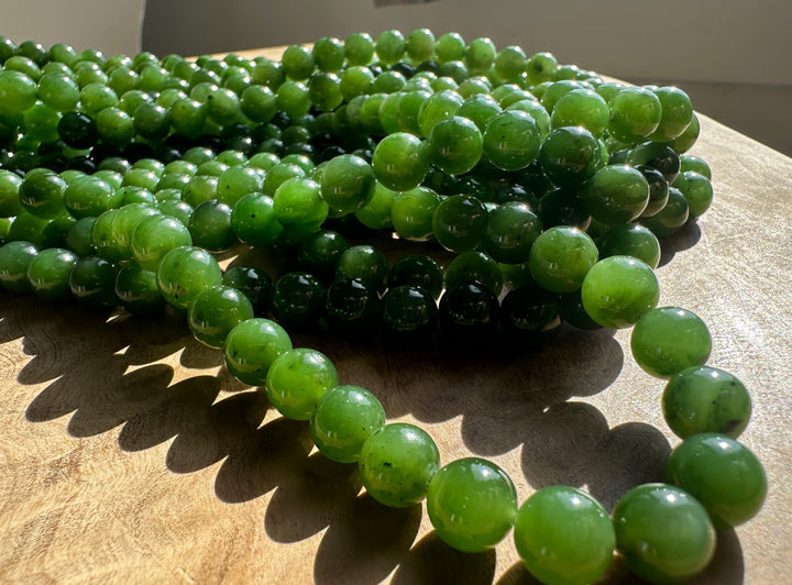 Green Canadian Nephrite Jade Unstrung Beads on a wooden base in sunlight
