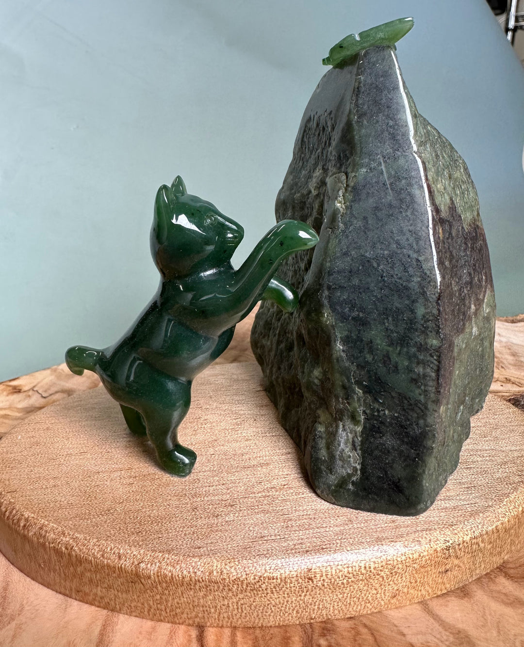 Green jade cat statue reaching toward a jade butterfly perched on a tall dark rock