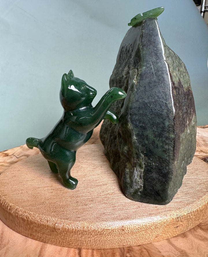 Green jade cat statue reaching toward a jade butterfly perched on a tall dark rock