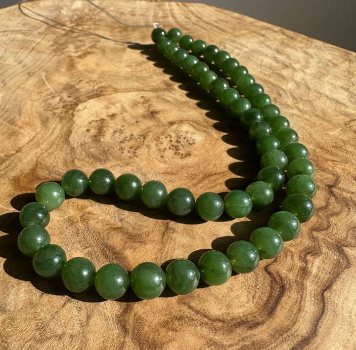 Green Canadian Nephrite Jade Unstrung Beads on a wooden base in sunlight