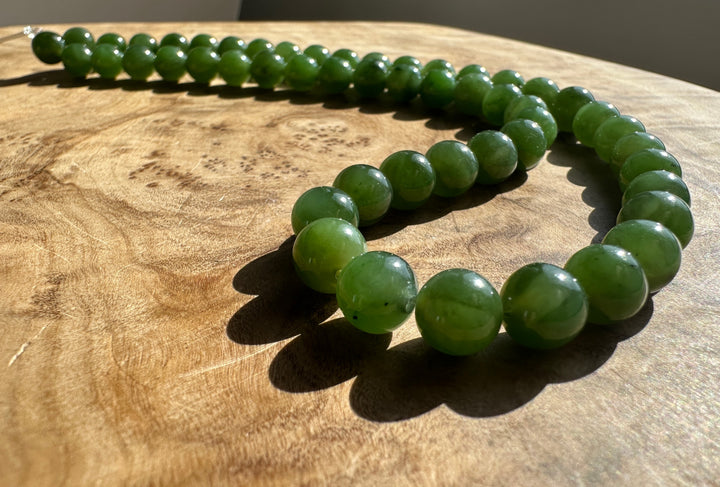 Green Canadian Nephrite Jade Unstrung Beads on a wooden base in sunlight
