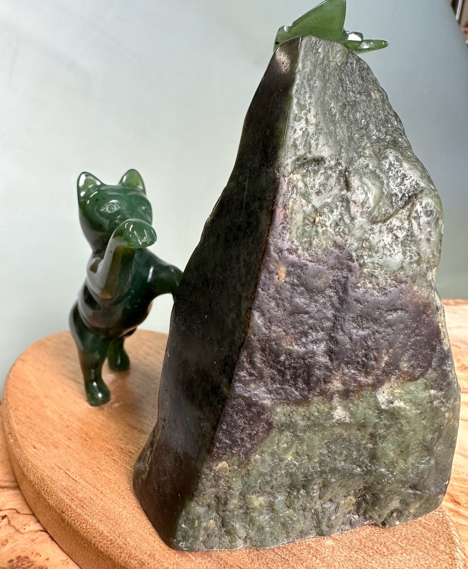 Green jade cat statue reaching toward a small jade butterfly perched on a tall rock.
