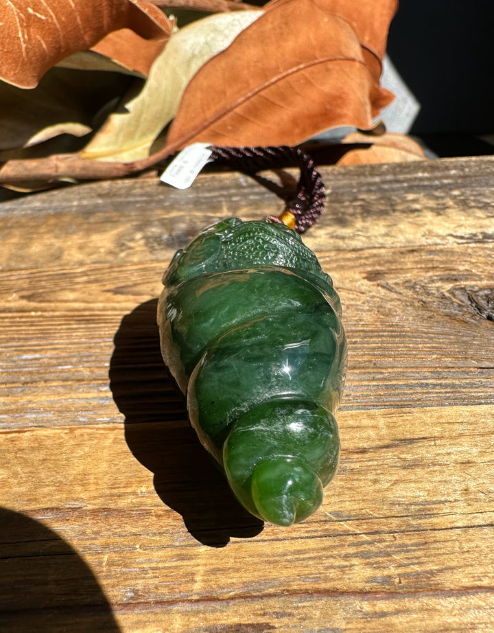 Toad in shell pendant carved from green stone with a dark braided cord resting on a wooden surface