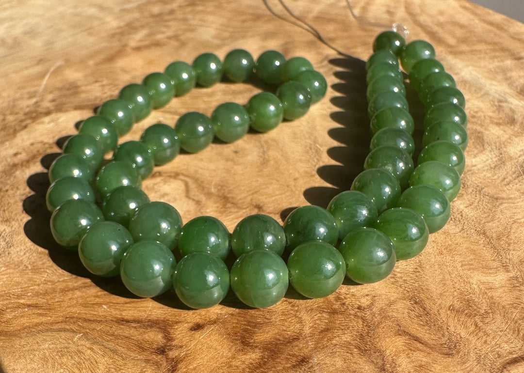 Green Canadian Nephrite Jade Unstrung Beads on a wooden base in sunlight