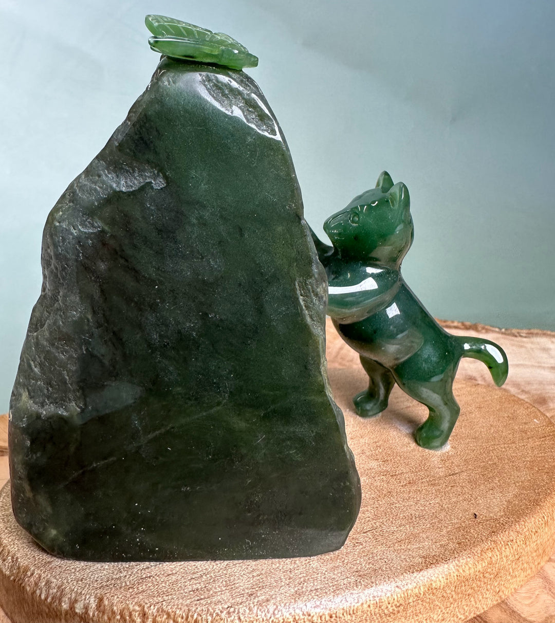 Green jade cat pawing at a small jade butterfly perched on a dark rock.