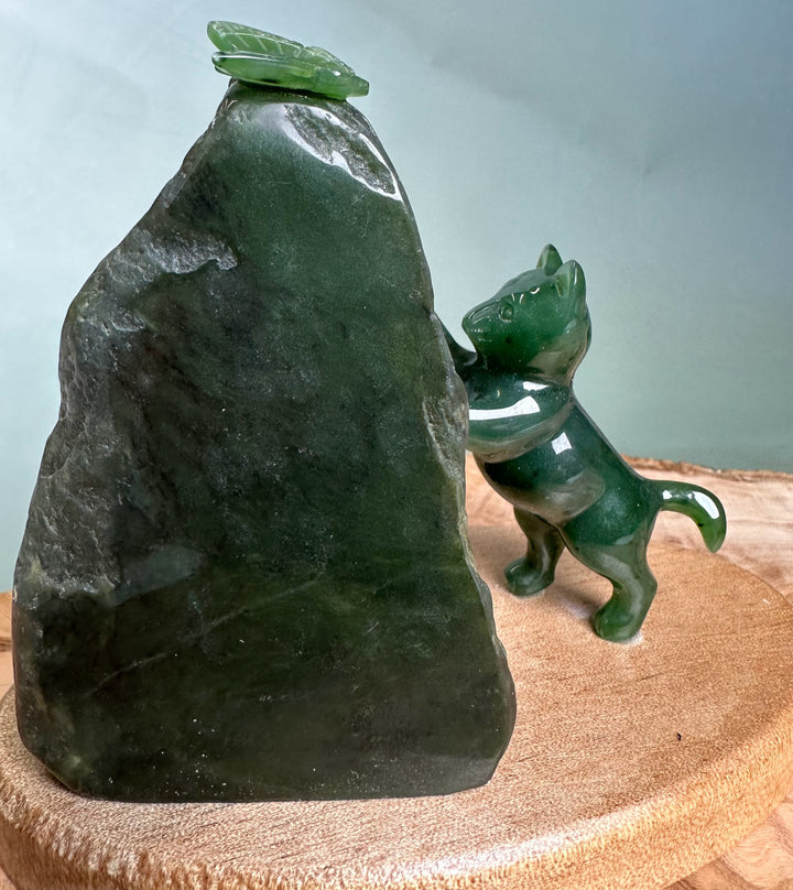 Green jade cat pawing at a small jade butterfly perched on a dark rock.