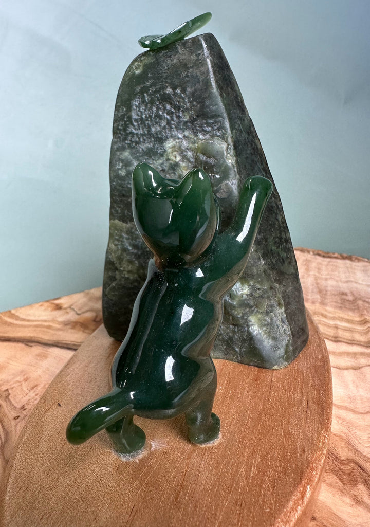 Green jade cat statue pawing at a jade butterfly atop a dark rock on a wooden base