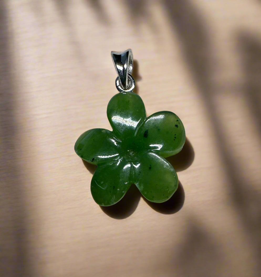 Green jade Forget Me Knot flower pendant with four-petaled petals and silver bail on beige backdrop.