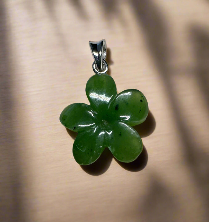 Green jade Forget Me Knot flower pendant with four-petaled petals and silver bail on beige backdrop.
