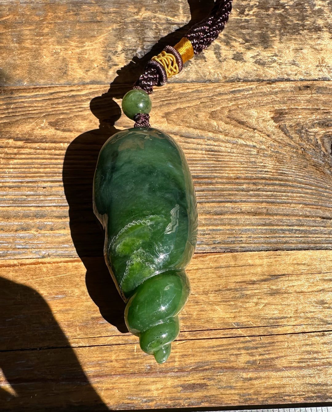 Top view of the green shell shaped pendant with a round bead on a braided cord against wood